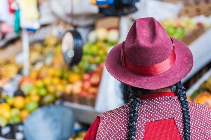 Eine Person mit roter Mütze und Zöpfen auf einem Markt voller Obst und Gemüse. 1