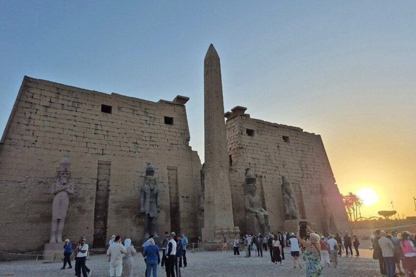 Un templo egipcio antiguo con un obelisco alto y estatuas, rodeado de turistas. 4