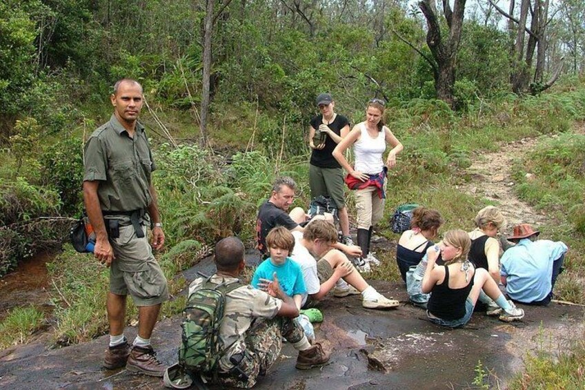 A group of people sitting on a wet stone path in a forested area. 1