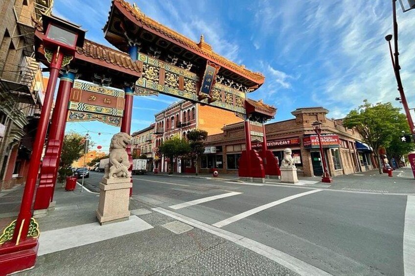 Une rue ornée d’une arche chinoise traditionnelle, d’une statue de lion et de bâtiments portant des enseignes. 2