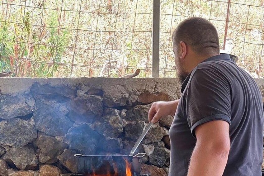 Una persona cucina all'aperto, con un muro in pietra e vegetazione sullo sfondo. 5