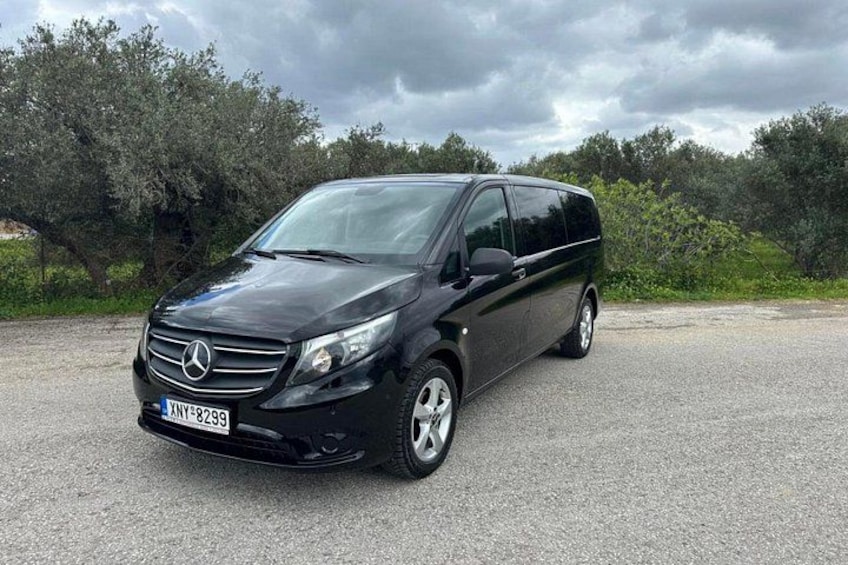 Un minivan Mercedes-Benz nero parcheggiato su un fondo ghiaioso, con alberi e cielo nuvoloso sullo sfondo. 2