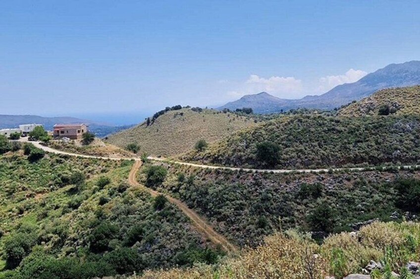 Una strada tortuosa che si snoda attraverso un paesaggio collinare, con poca vegetazione e una vista lontana delle montagne. 1
