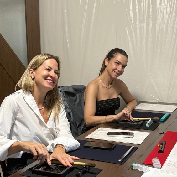 Two individuals seated at a table with various office supplies and documents. 3