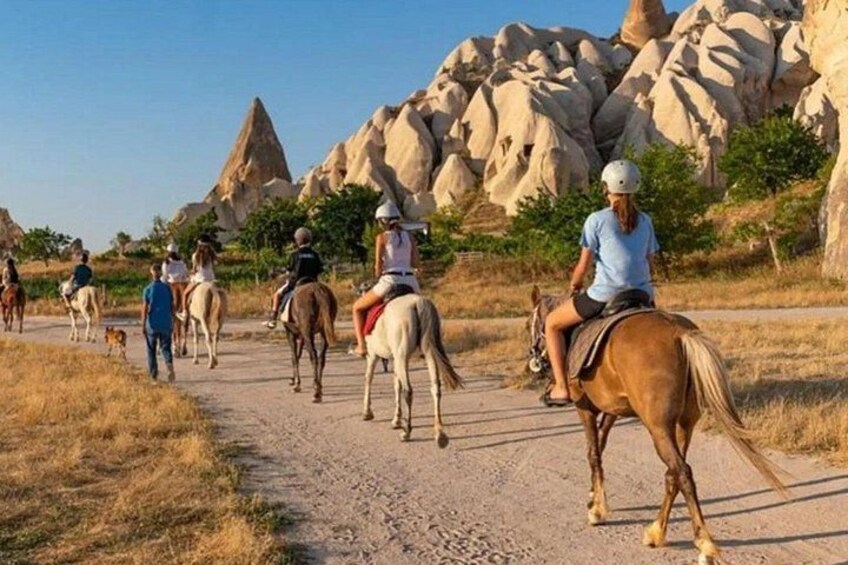 Un grupo de personas montando a caballo por un sendero de tierra con formaciones rocosas al fondo. 1