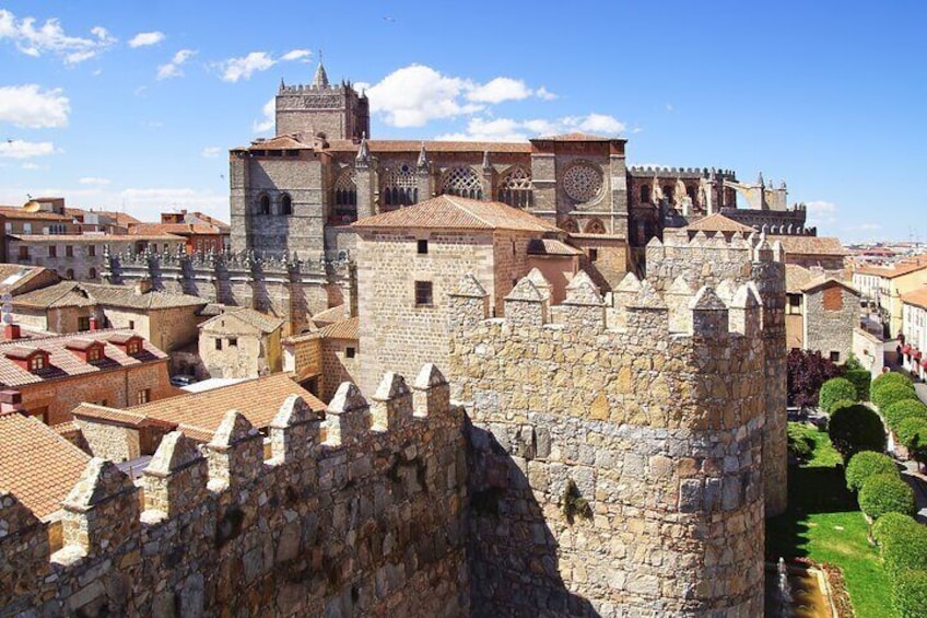 A historic stone fortress with battlements, a clock tower, and a cathedral in the background. 3