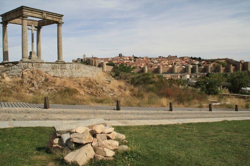 Ancient ruins with columns, a stone pile, and a distant cityscape. 4