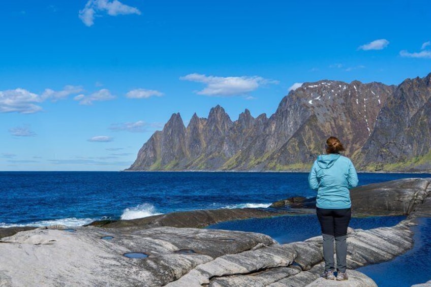 Une personne se tient debout sur un promontoire rocheux au bord de la mer, avec un paysage montagneux en arrière-plan. 1