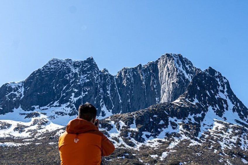 A person in an orange jacket standing in front of a snow-covered mountain. 5