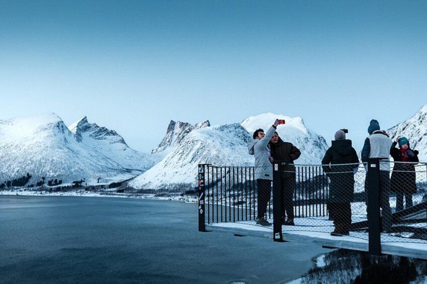 A group of people standing on a bridge overlooking a frozen lake with mountains in the background. 2