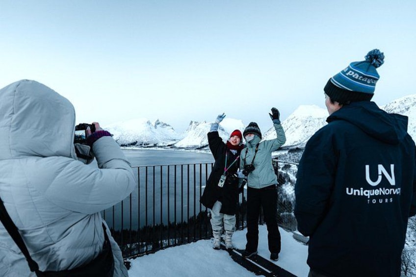 A group of people on a snowy mountain, some taking photos, with a clear sky and snow-covered peaks in the background. 3