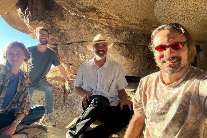 Four people sitting and standing on a rocky outcrop with a large rock formation in the background. 5