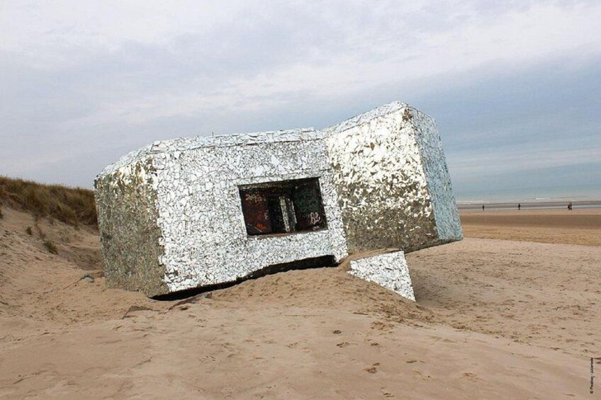 A large, silver-coated structure resembling a house on a sandy beach with a clear sky. 4
