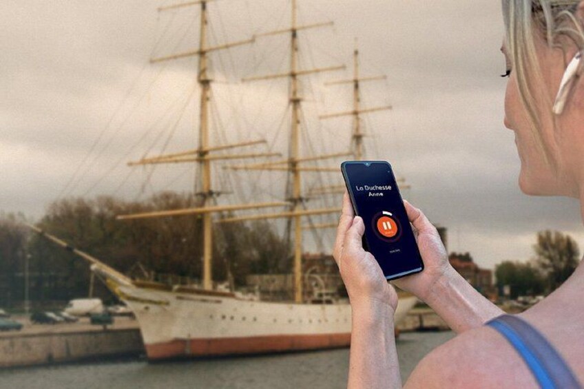 A person holding a smartphone with a music app open, a large sailing ship in the background, and a cloudy sky. 5