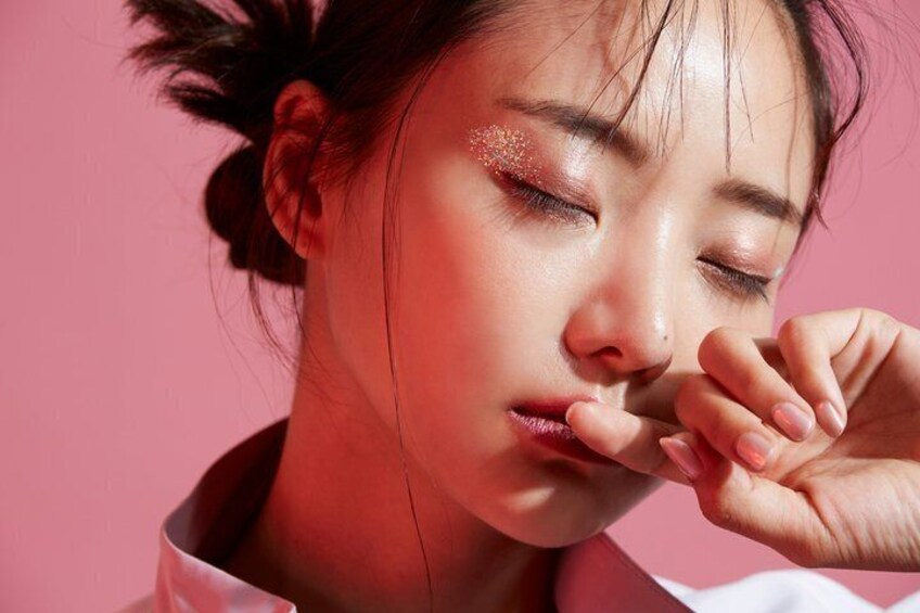 Une personne coiffée avec un chignon, portant un vêtement rose, sur un fond rose. 1