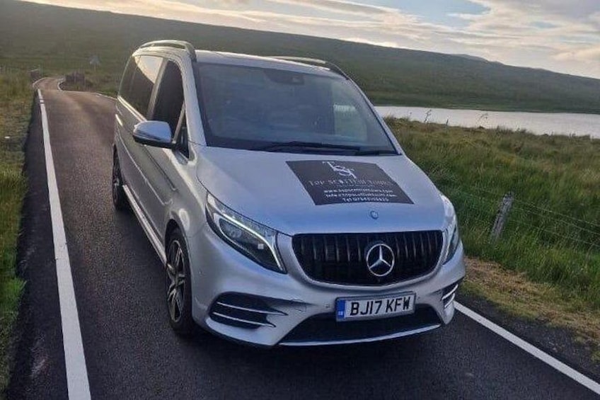 Un SUV Mercedes-Benz plateado en una carretera, con un área verde y un cuerpo de agua al fondo. 3