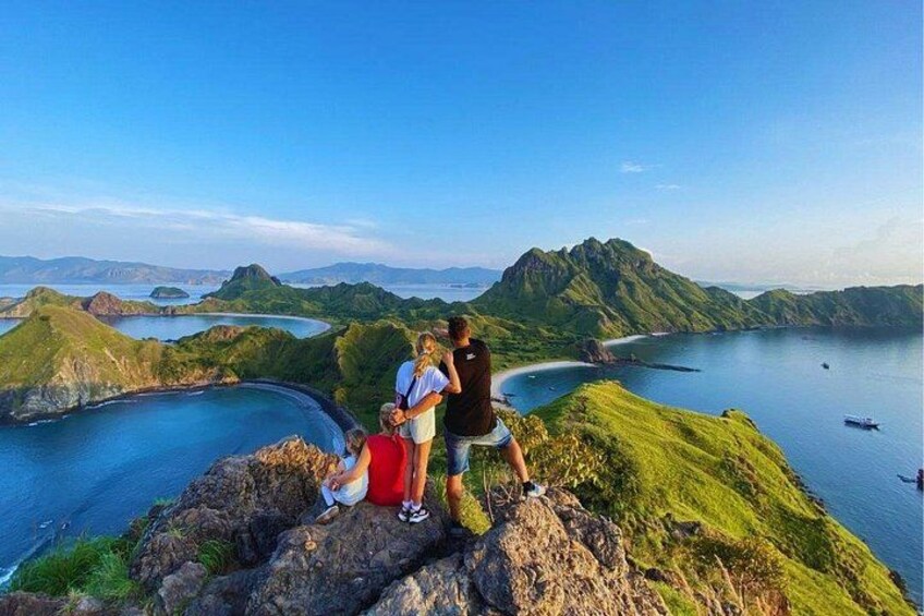 A group of people on a rocky outcrop overlooking a bay with green hills and a clear blue sky. 1