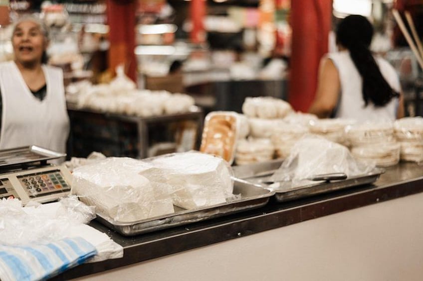 A bakery counter with bread and pastries, a cash register, and a weighing scale. 2