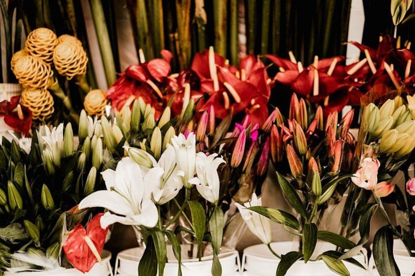 A variety of flowers including lilies and red and pink blooms, arranged in a market setting. 3