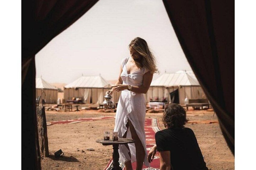 A person in a white dress standing in a tented area with a table and chairs. 1