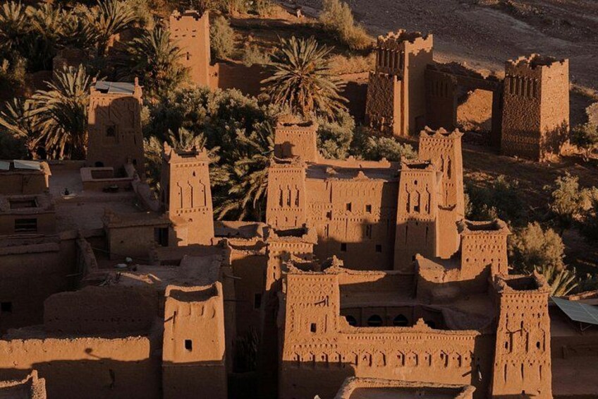 A traditional mud-brick village with multiple towers and palm trees. 5