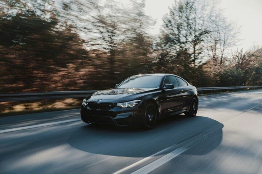 A black car driving on a road with trees in the background. 3