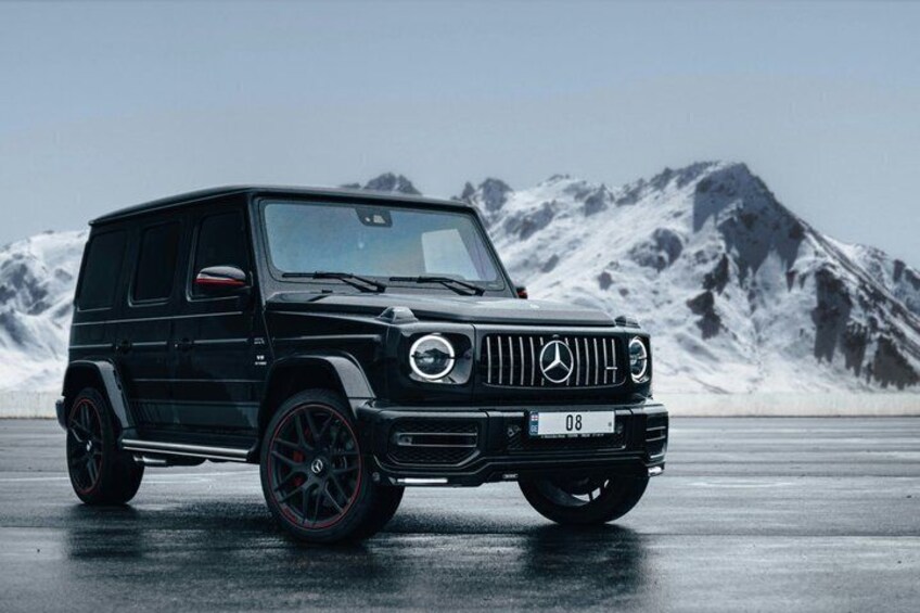A black Mercedes-Benz G-Class SUV parked on a wet surface with a mountainous background. 2
