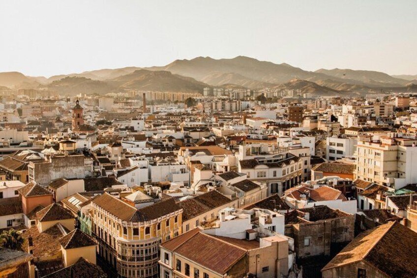 Un paisaje urbano con un edificio curvo destacado, una torre y una cadena montañosa al fondo. 4