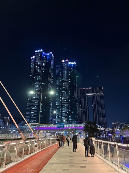 A nighttime cityscape with illuminated high-rise buildings and a pedestrian walkway. 2