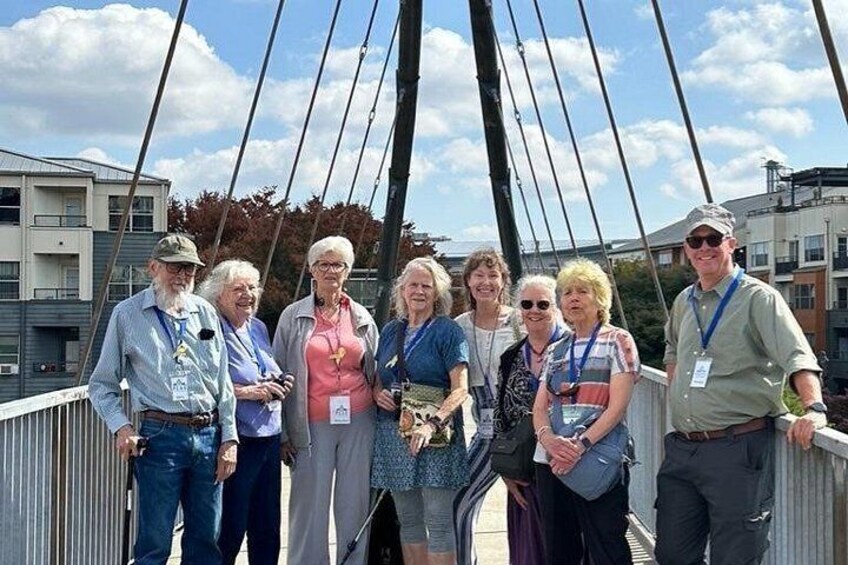 A group of people standing on a bridge with a metal railing, buildings in the background, and a clear sky. 4