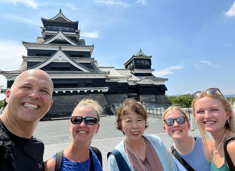 A group of people standing in front of a traditional Japanese castle with multiple tiers and a prominent tower. 1