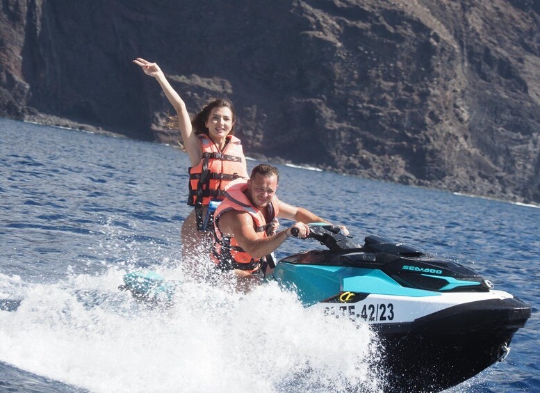 A person riding a jet ski on a body of water with a rocky coastline in the background. 2