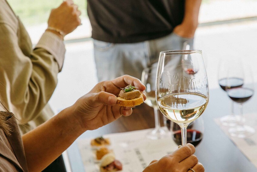 A person holding a small appetizer and a glass of white wine. 5