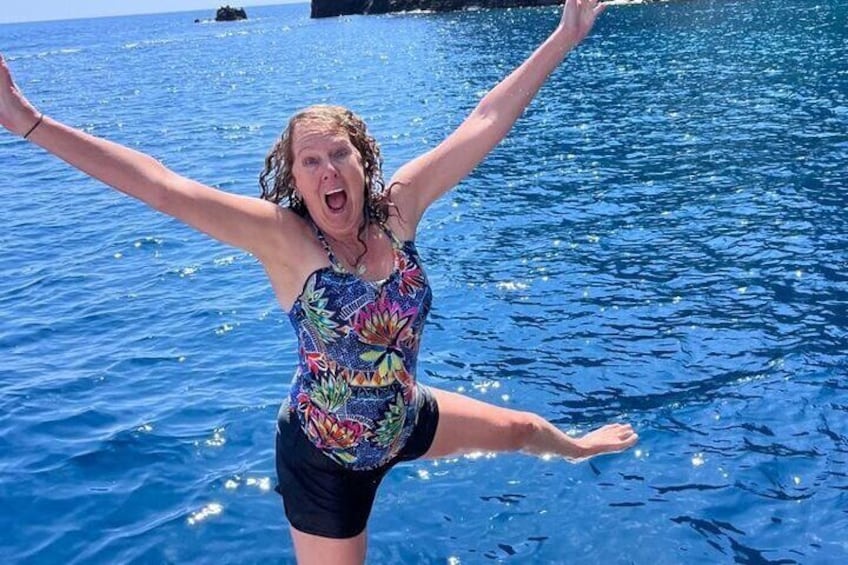 A person in a colorful swimsuit standing in water with arms raised. 1