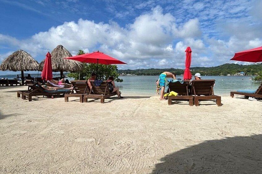 Een strand met ligbedden en rieten parasols. 5