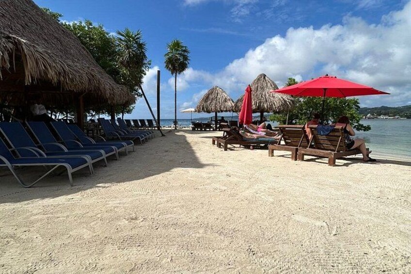 Een strand met rieten hutten, ligbedden en parasols. 4
