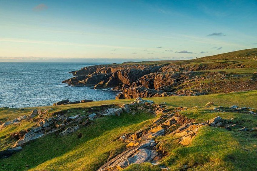 A coastal landscape with rocky cliffs, grassy terrain, and a view of the sea. 3