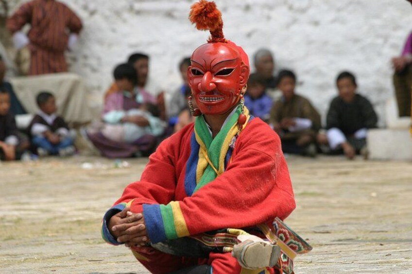 A person in traditional attire with a red headpiece sitting on the ground. 1