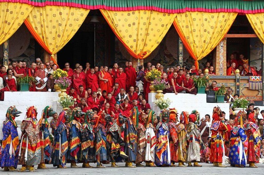 A group of people in colorful traditional attire, some in red robes, gathered in an outdoor setting with a stage and draped yellow and red fabric. 4