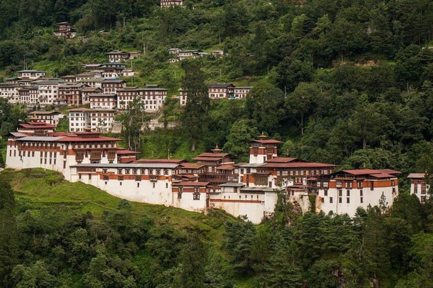 A monastery complex with multiple buildings, surrounded by lush greenery and hills. 2