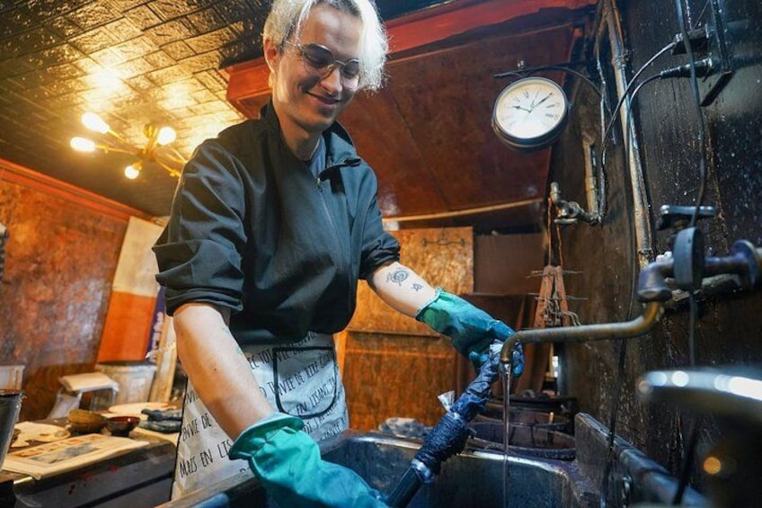 A person working with a large machine, wearing gloves and an apron, in a workshop with wooden walls and a clock. 5