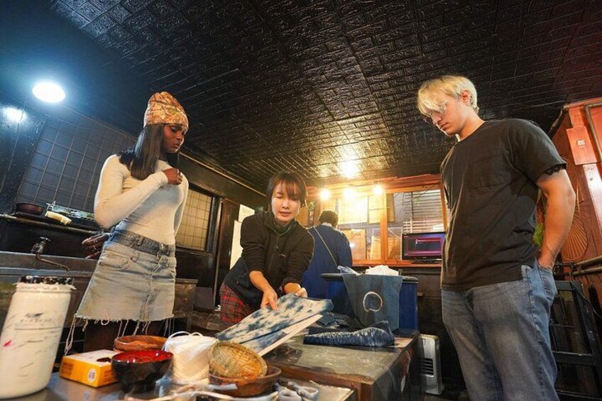 A group of people in a dimly lit room with a brick ceiling, surrounded by various items like a large container, a box, and some tools. 2