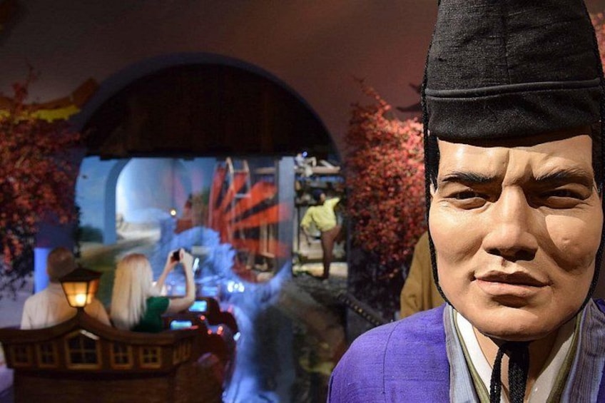 A person in a purple jacket and a black hat, with a blurred background featuring a traditional building and cherry blossoms. 3