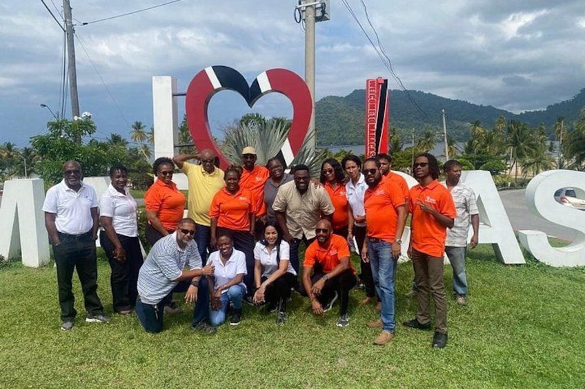 A group of people posing in front of a large heart-shaped sign with the letters 'MAS' visible. 2