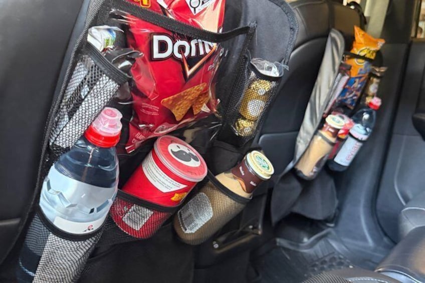 A car's center console with a storage organizer containing snacks, drinks, and a bottle of water. 3