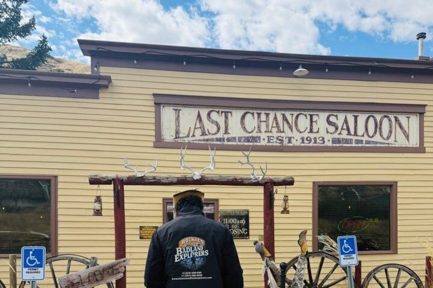 A building with a sign reading 'LAST CHANCE SALOON EST. 1913' and a disabled parking sign. 2
