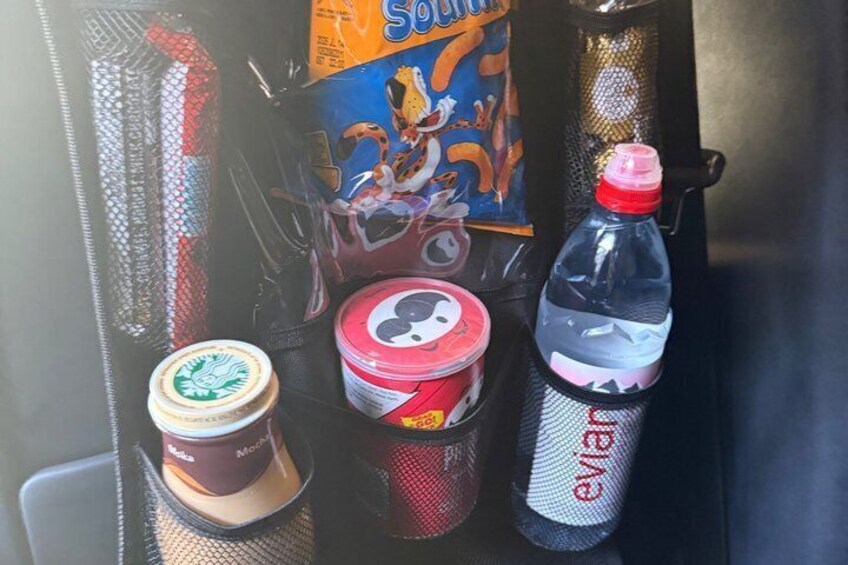 Une sélection de boissons et d’en-cas à disposition dans le véhicule, comprenant un gobelet Starbucks, une boîte de chips Pringles et une bouteille d’eau Evian. 3