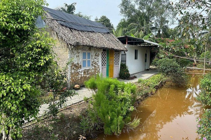 A rural house with a thatched roof, a small garden, and a muddy stream. 1