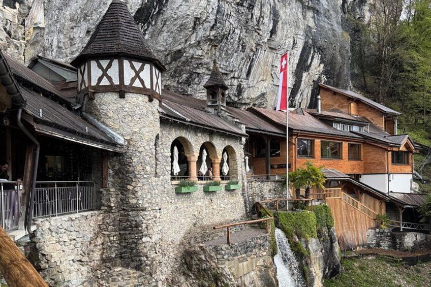 Una cabaña de montaña con paredes de piedra, balcones de madera y una cascada. 4