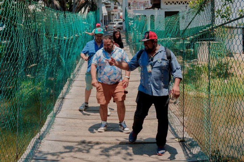 A group of people walking on a pedestrian bridge with a green net fence on one side. 2